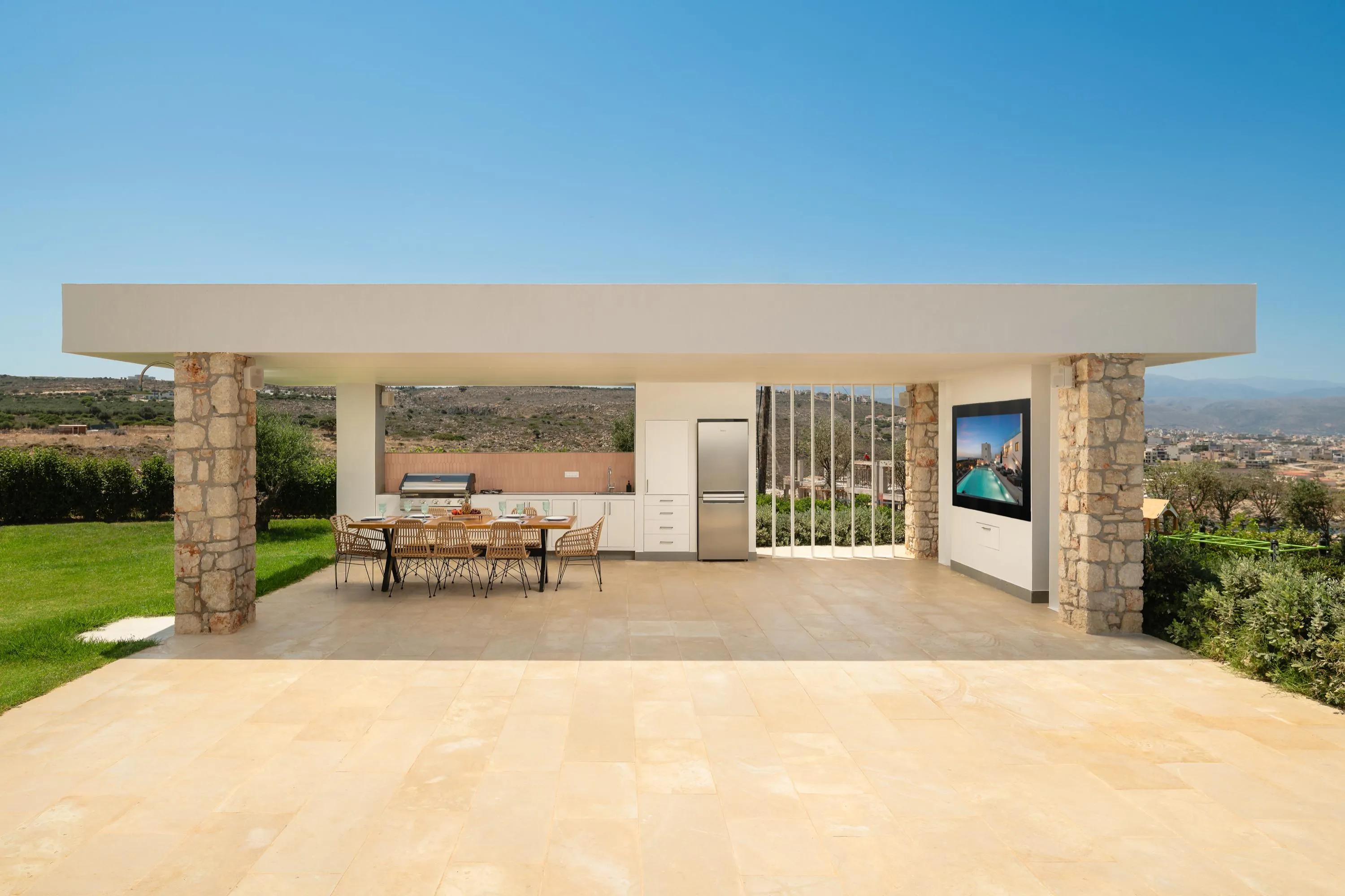 A fully equipped outdoor BBQ area under a shaded pergola — complete with a gas BBQ, gas stove, fridge, spacious dining table, and large TV — is the perfect place to gather with family and friends.