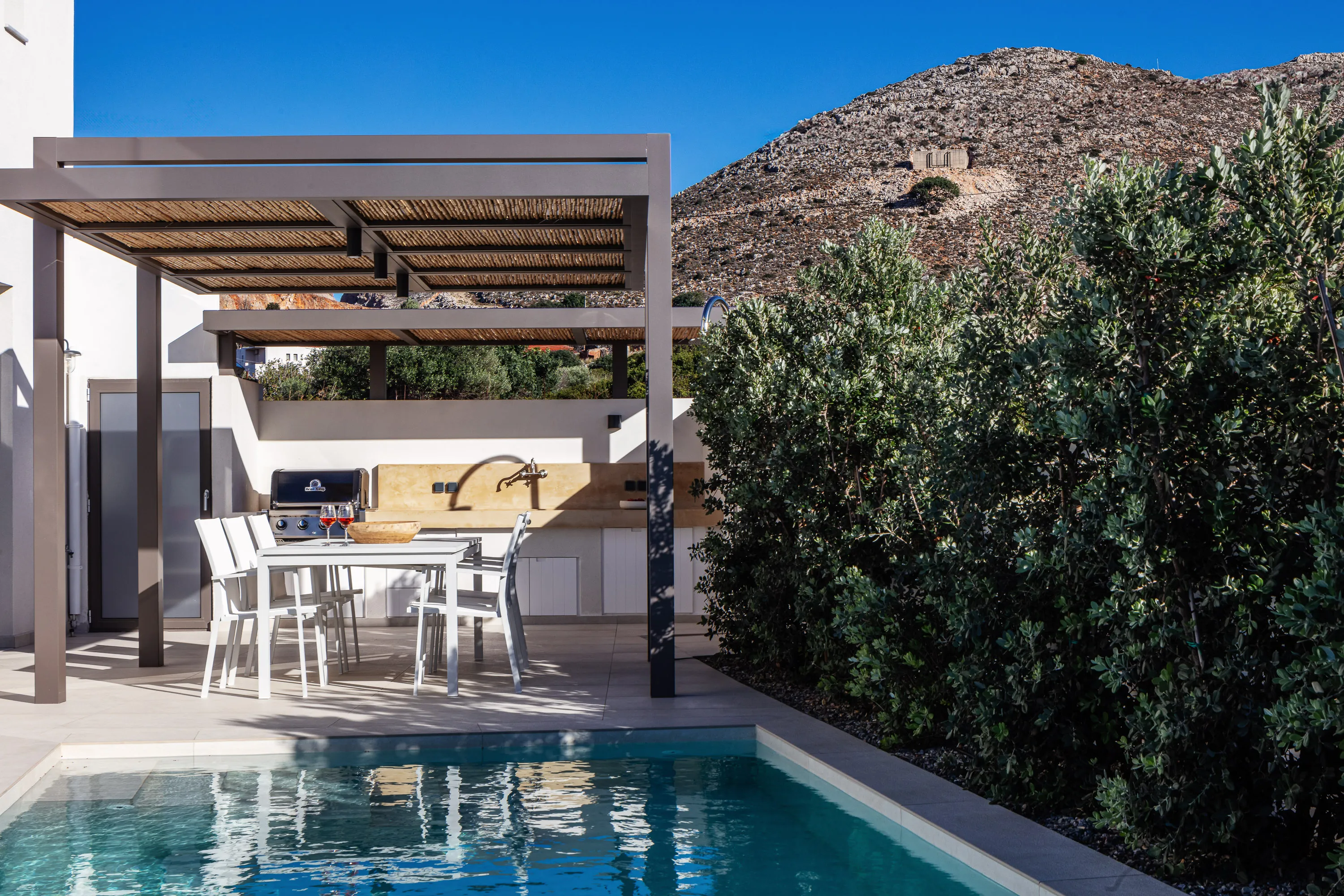 There is an outdoor dining area under the pergola next to the pool