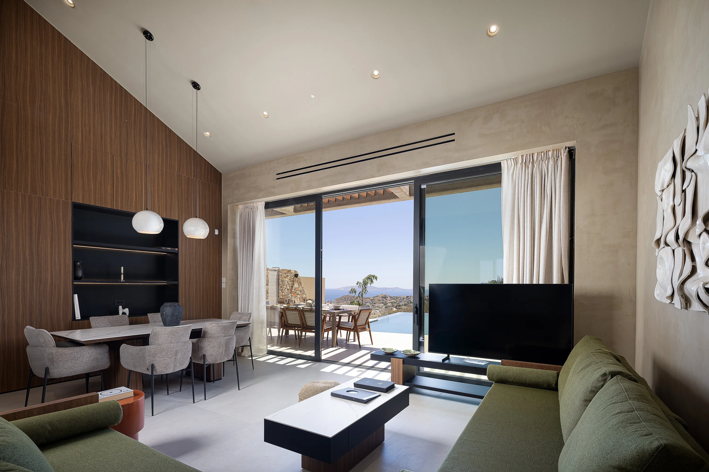 The open-plan living area features modern design, a 65” Smart TV, JBL speaker, and direct access to the pool terrace. A bright, stylish space designed for relaxation with stunning sea views.